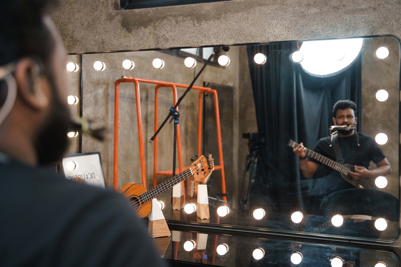 Gladson Peter rehearsing in a mirror-lined green room with harmonica rig and guitar